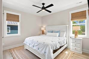 A bedroom with a bed, bedside tables, a ceiling fan, and windows with blinds.