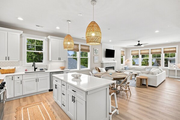 A spacious kitchen with white cabinetry, a central island, and a dining area with wicker chairs.