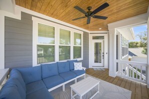 A covered porch with a blue sofa, a small table, and a ceiling fan.