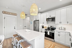 A modern kitchen with white cabinetry, a central island, stainless steel appliances, and wicker pendant lights.