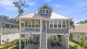 A two-story house with a covered porch, a staircase leading to the upper level, and a number '106' on the front wall. - Anchor Forty-Five: Coastal home with large deck, close to beach and local attractions (Oak Island)