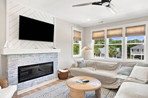 A modern living room with a fireplace, a large flat-screen TV, a sofa, and a ceiling fan.