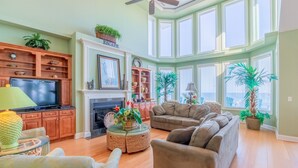 A spacious living room with a fireplace, comfortable seating, and large windows. - Oceanfront, multi-level home with beach access, views, game room, & elevator (North Topsail Beach)