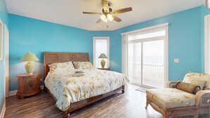 A bedroom with a bed, a chair, a ceiling fan, and a window. - Oceanfront, multi-level home with beach access, views, game room, & elevator (North Topsail Beach)