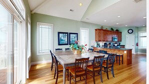A spacious kitchen with wooden cabinets, a central island, and a dining area with a large table and chairs. - Oceanfront, multi-level home with beach access, views, game room, & elevator (North Topsail Beach)