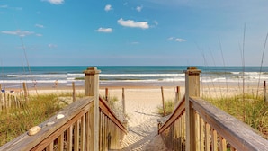 A wooden boardwalk leading to a beach with clear skies and ocean waves. - Live Like Royalty in This 9-Bedroom Oceanfront Retreat (North Topsail Beach)
