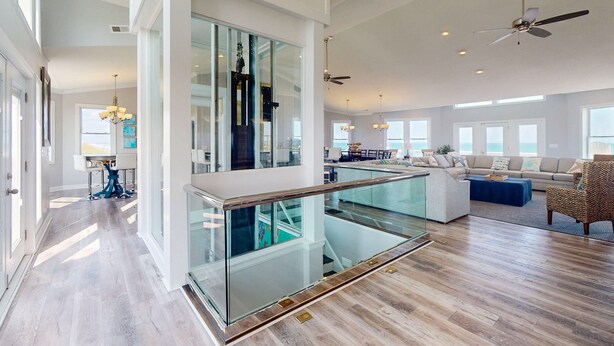 A spacious living area with a glass railing, a sofa set, and a ceiling fan. - Live Like Royalty in This 9-Bedroom Oceanfront Retreat (North Topsail Beach)