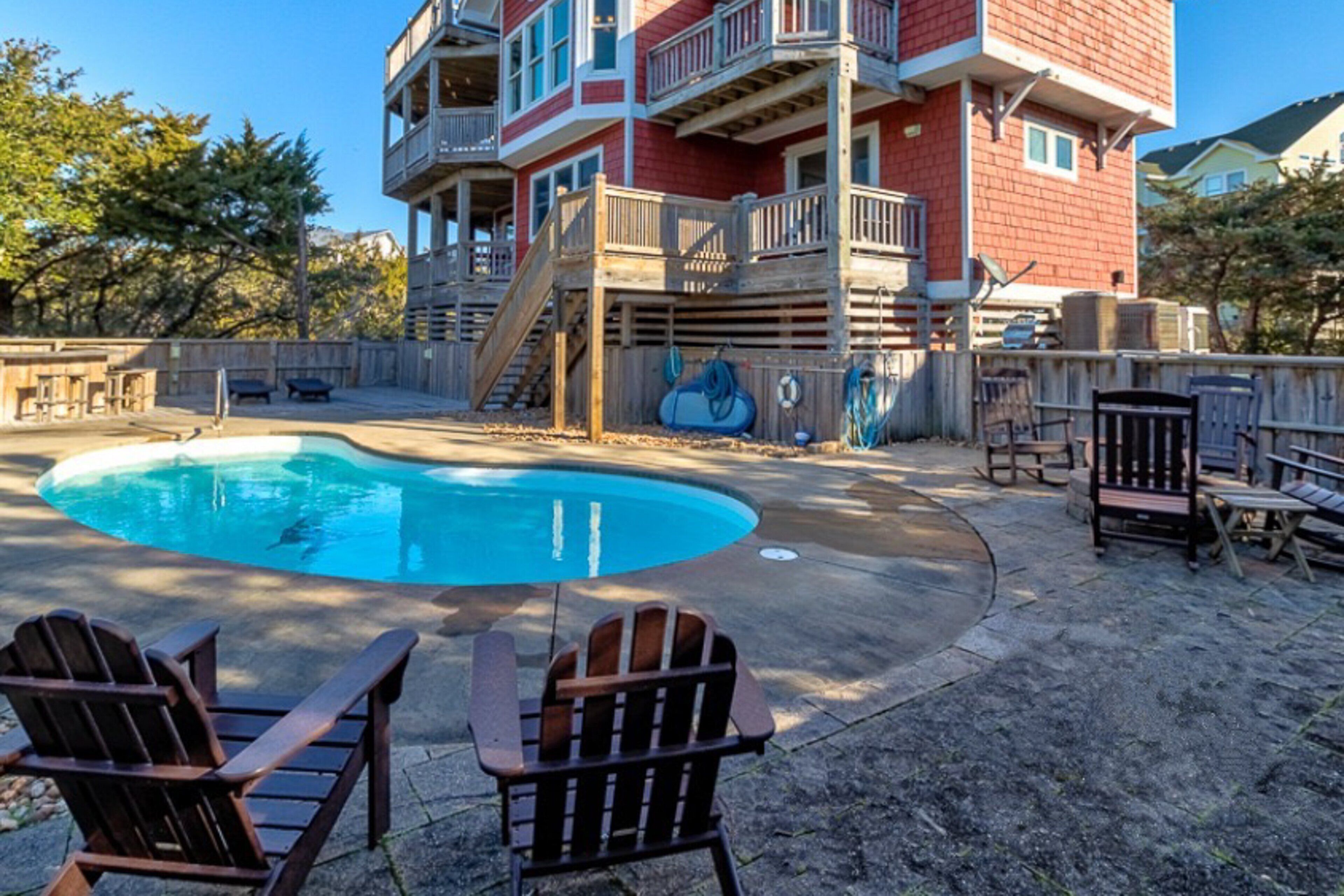 A backyard with a swimming pool, wooden deck, and Adirondack chairs.