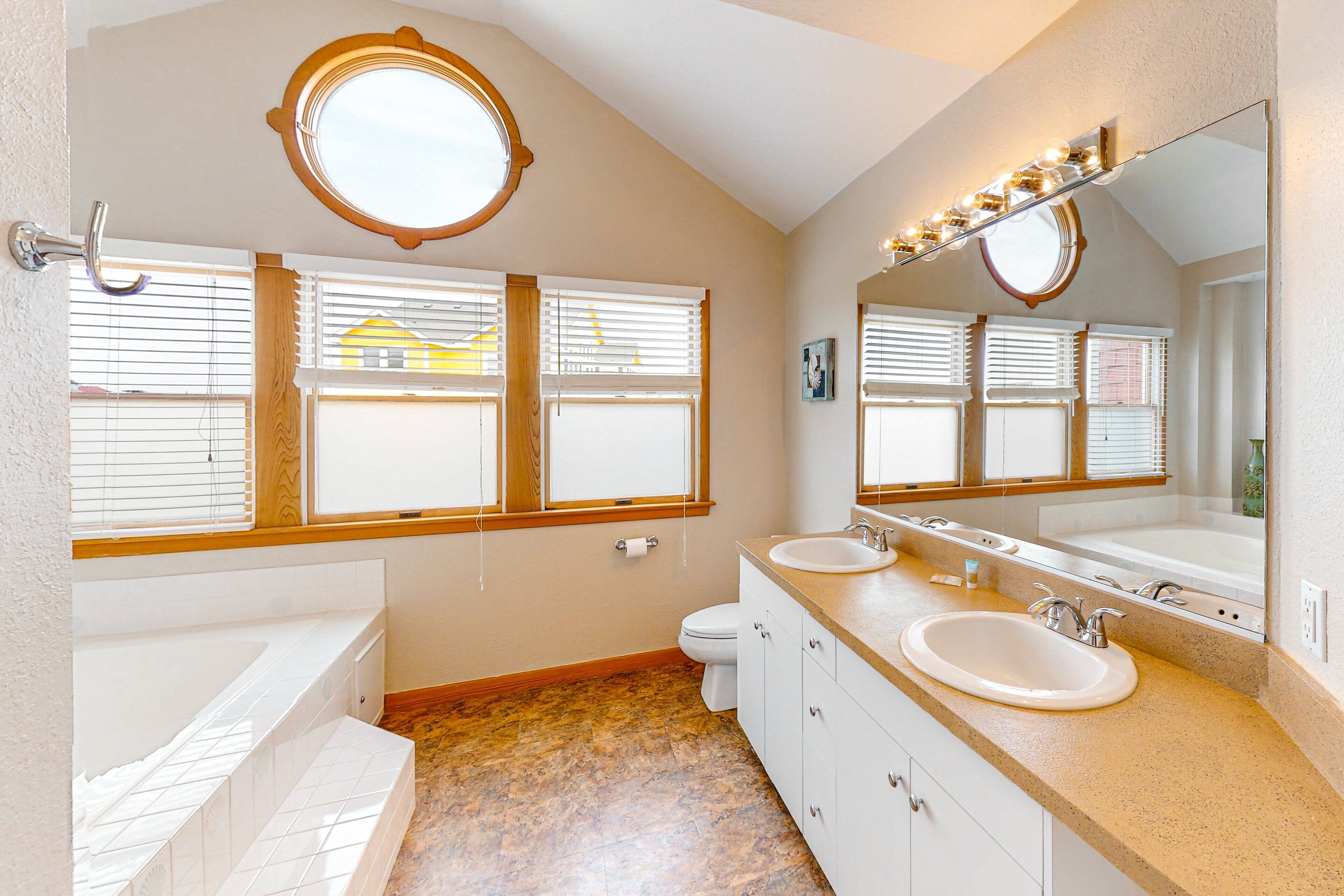 A bathroom with a bathtub, two sinks, a toilet, and a large mirror with lights.