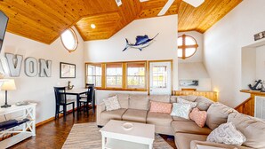 A cozy living room with a large sofa, a coffee table, and a dining area with a table and chairs. - Reel 'Em Inn 403: Gorgeous, outdoor pool, spacious carport, decks (Avon)