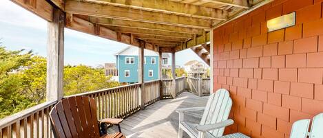 A wooden deck with two Adirondack chairs and a bench, overlooking a residential area with houses.