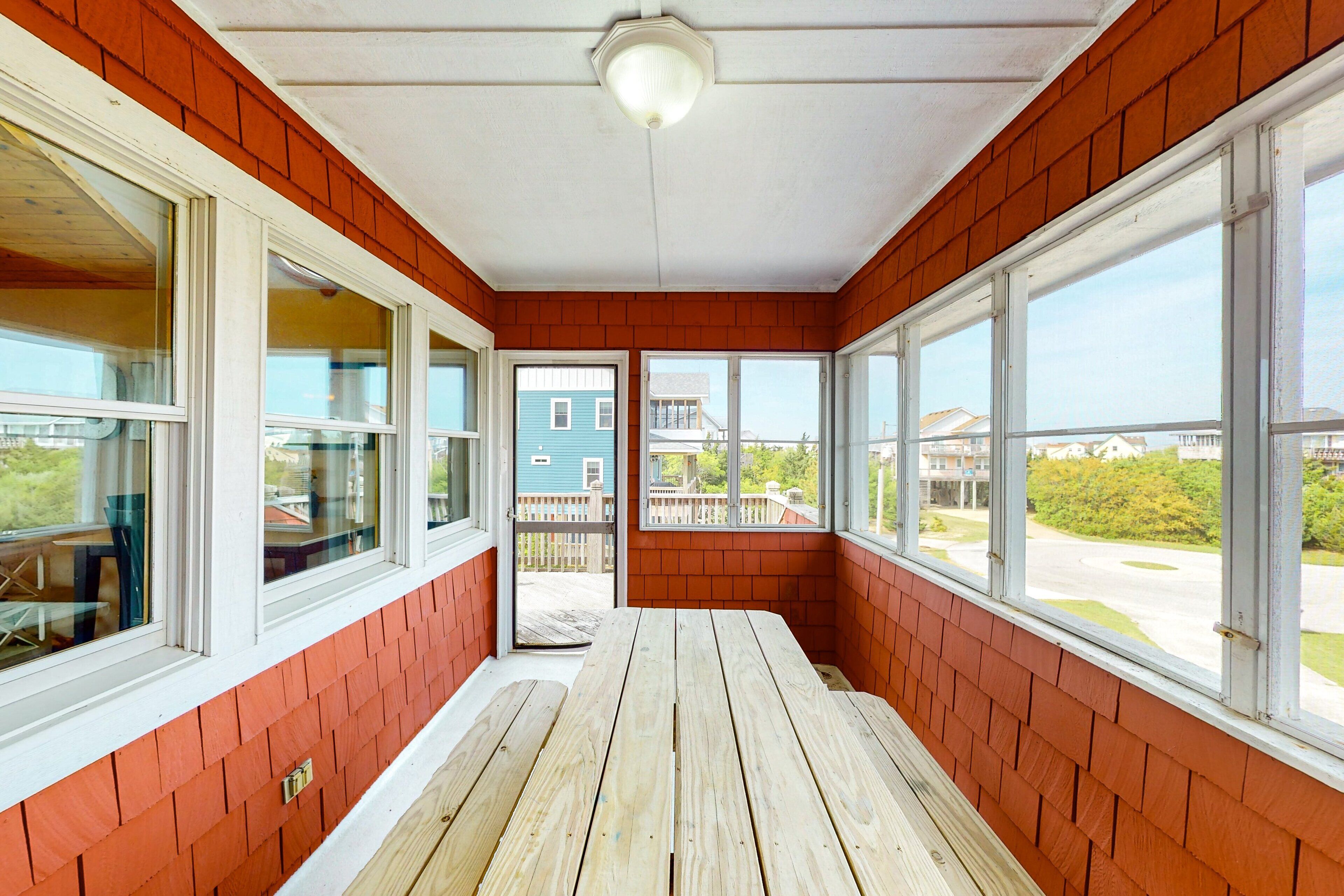 A sunroom with large windows, a wooden bench, and a view of neighboring houses.