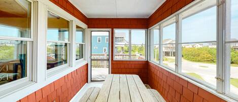 A sunroom with large windows, a wooden bench, and a view of neighboring houses.