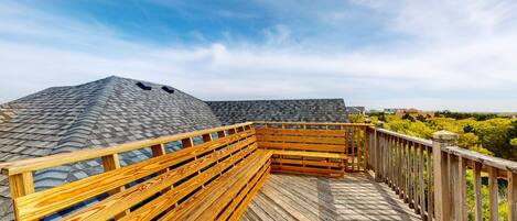 A wooden deck with a bench, overlooking a residential area with houses and trees.