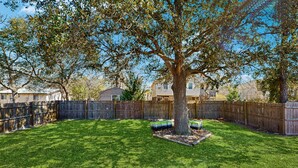 Un jardin avec un grand arbre, une clôture en bois et une pelouse bien entretenue.