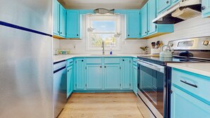 Une cuisine avec des armoires turquoise, une fenêtre et un réfrigérateur en acier inoxydable.