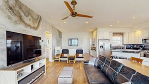 A modern living room with a large TV, leather sofa, and a dining area with a wooden table.