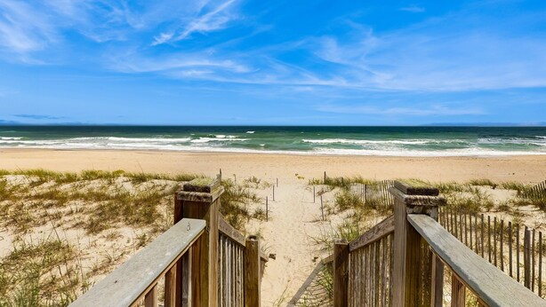 A wooden boardwalk leading to a sandy beach with ocean waves in the background.