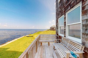 A wooden deck with a bench overlooking a grassy area and the ocean. - Reel Living #3-AV: Dog-Friendly, Waterfront Home, Hot Tub (Avon)