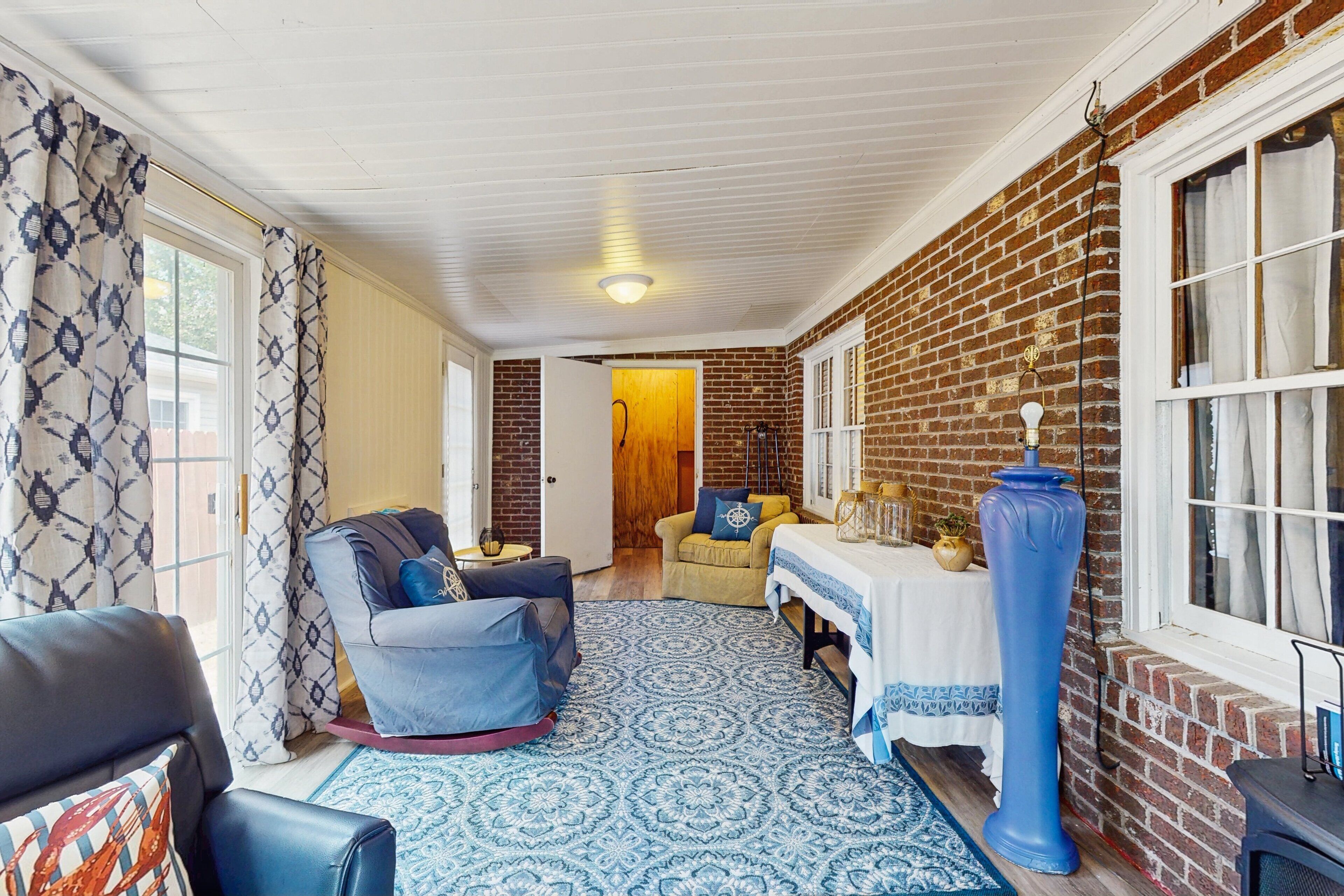Una sala de estar acogedora con un tapete azul estampado, un sofá de cuero, un sillón azul y una mesa con mantel blanco.