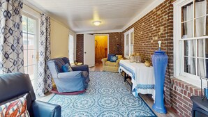 Ein gemütliches Wohnzimmer mit einem blauen Teppich mit Muster, einer Ledersofa, einem blauen Sessel und einem Tisch mit weißem Tischlauf.