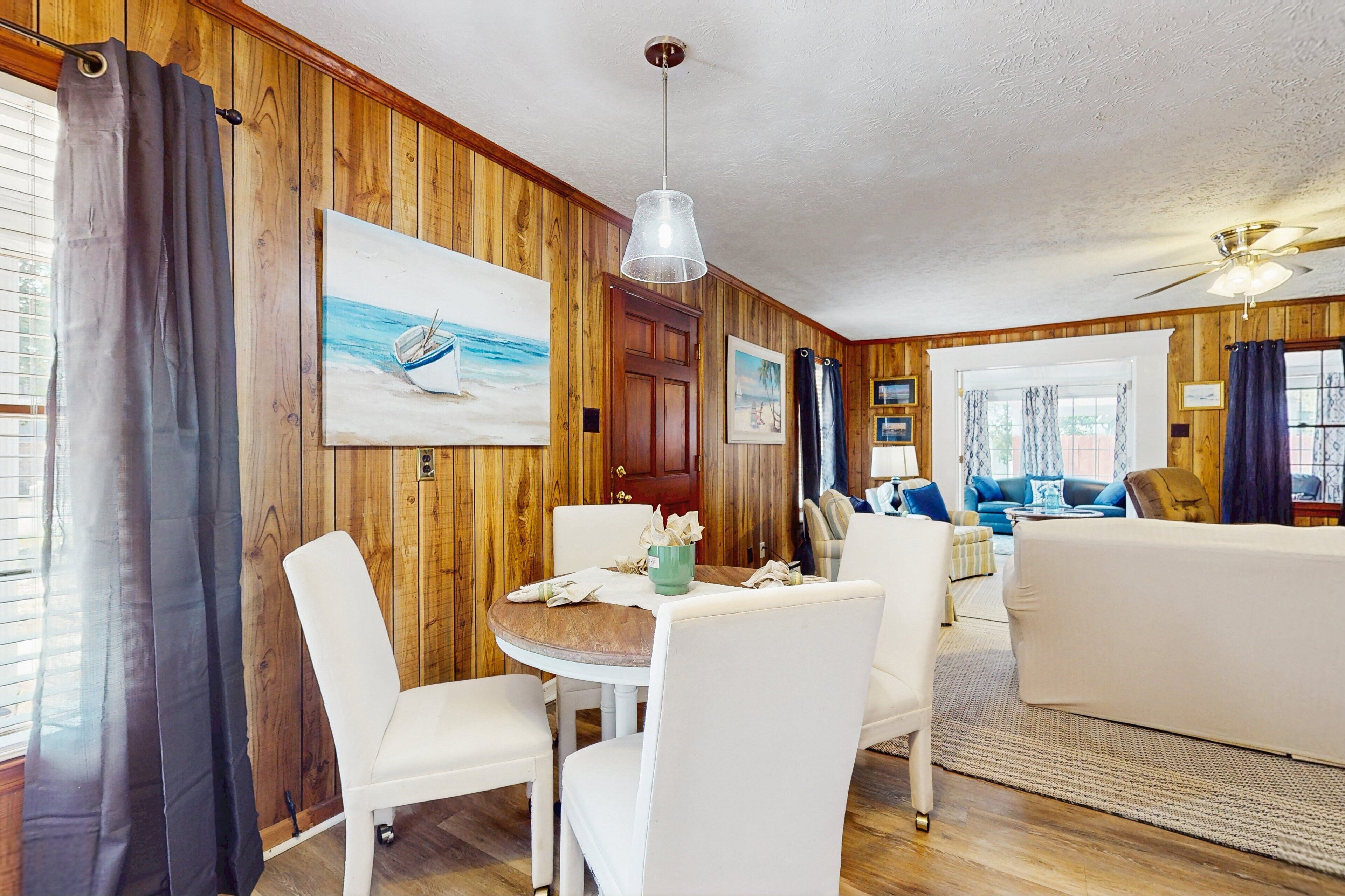 A cozy room with wooden walls, a dining table with chairs, a sofa, and a ceiling fan.