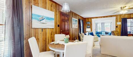 A cozy room with wooden walls, a dining table with chairs, a sofa, and a ceiling fan.