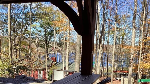 Un patio al aire libre con una larga mesa de madera y sillas, rodeado de árboles y vistas a un cuerpo de agua.