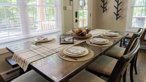 Un comedor con una larga mesa dispuesta para seis personas, con camino de mesa de cuadros, sillas de madera y un centro decorativo.