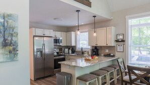 Una cocina moderna con electrodomésticos de acero inoxidable, una isla central con taburetes de bar e iluminación colgante.