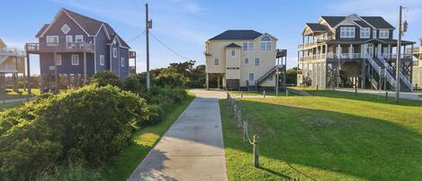 A residential street with houses, a sidewalk, and a grassy area.