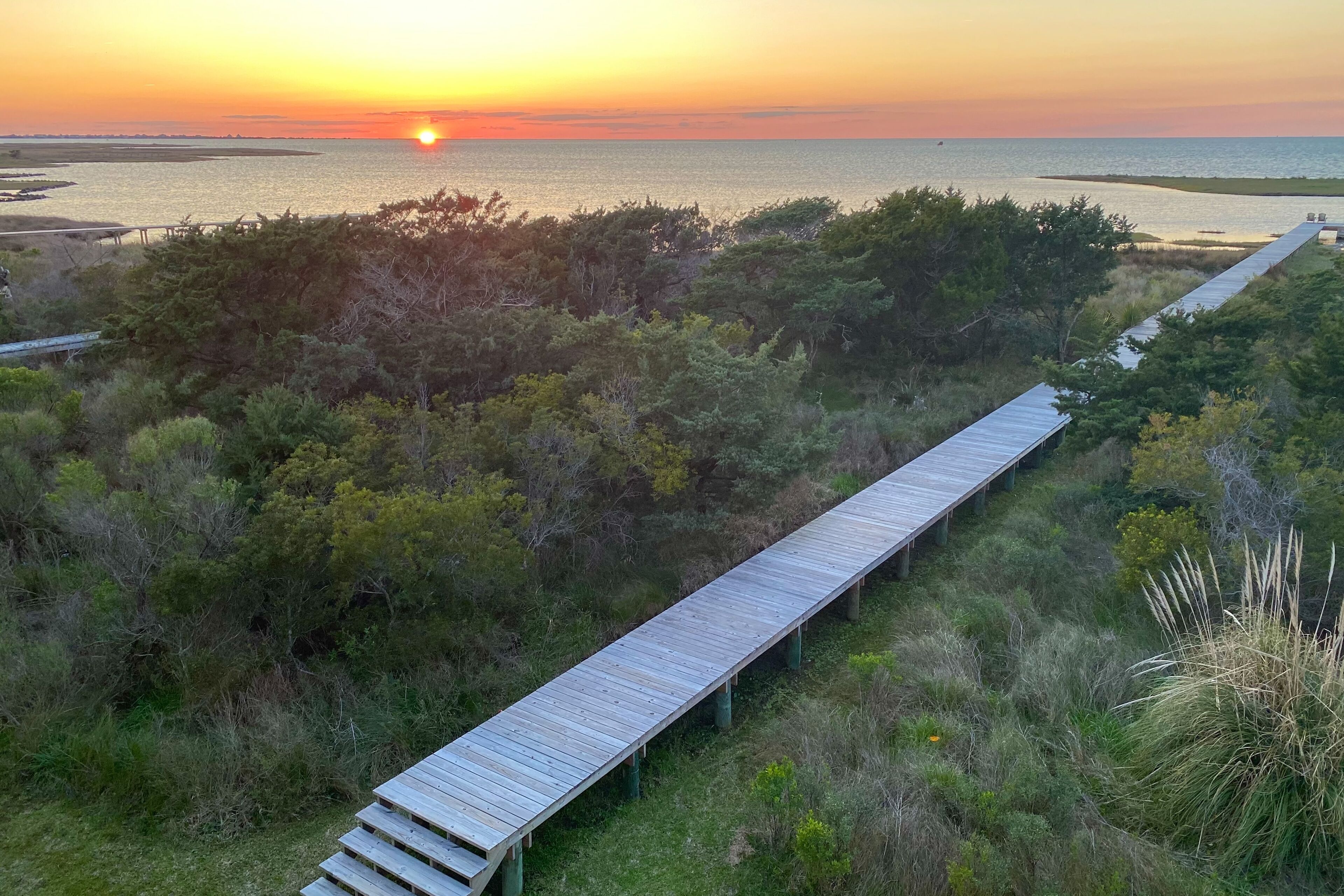 A wooden boardwalk leading to a beach with a sunset in the background.