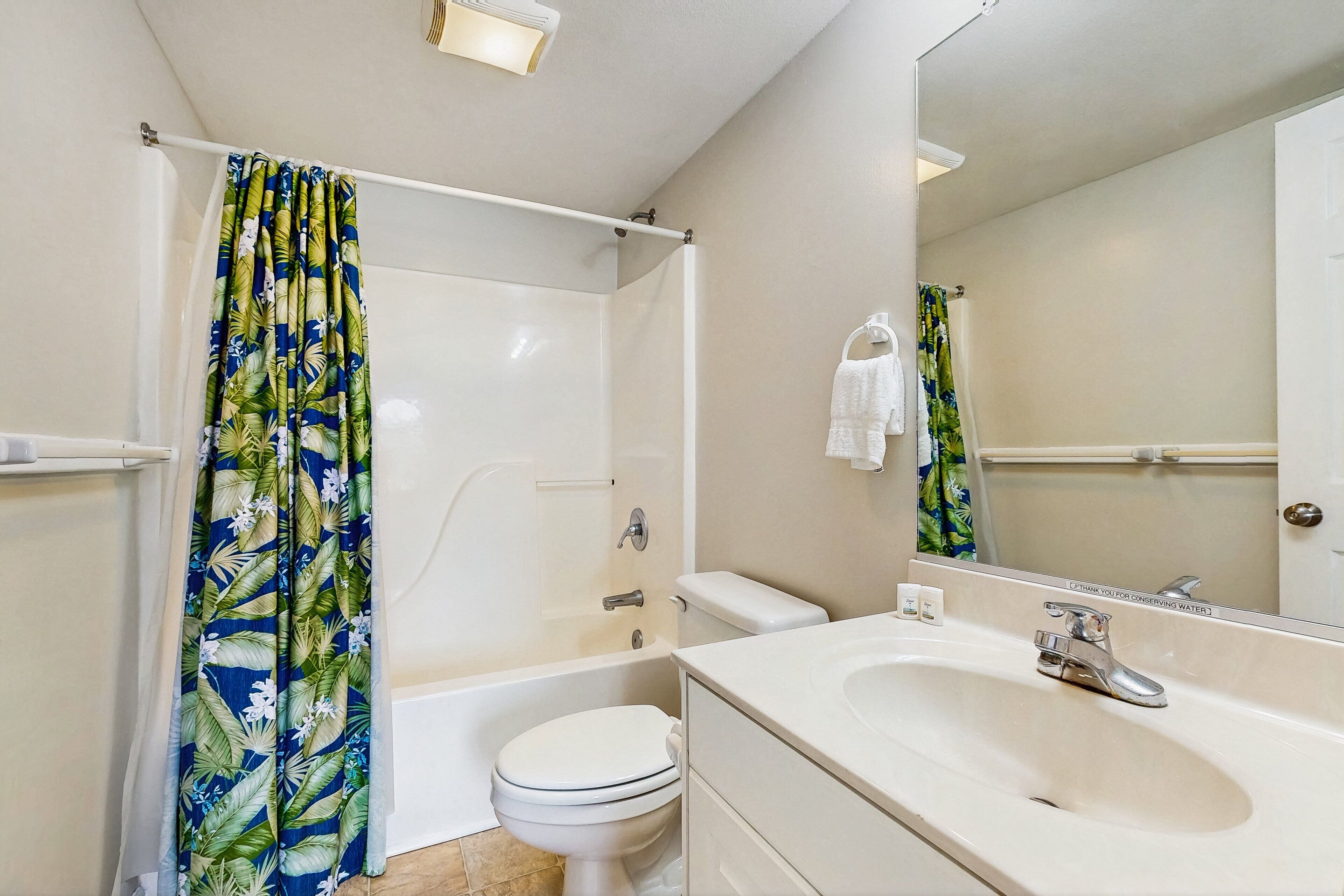 A bathroom with a bathtub, toilet, sink, and a shower curtain with a tropical leaf pattern.