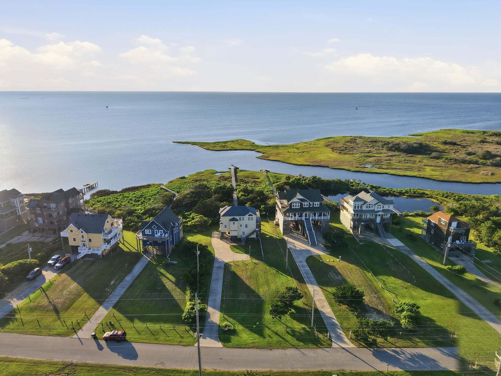 An aerial view of a coastal residential area with houses, a dock, and a clear view of the sea.