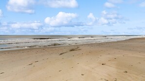 Een strand met voetafdrukken die naar het water leiden, een heldere lucht en een kalme zee.