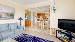 Een woonkamer met een bank, een televisie en een eethoek met stoelen en een tafel.