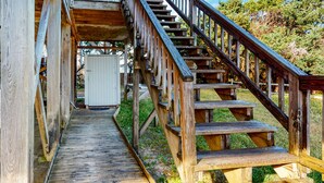 Eine Holztreppe führt zu einer überdachten Terrasse mit Blick auf ein Gebäude im Hintergrund.