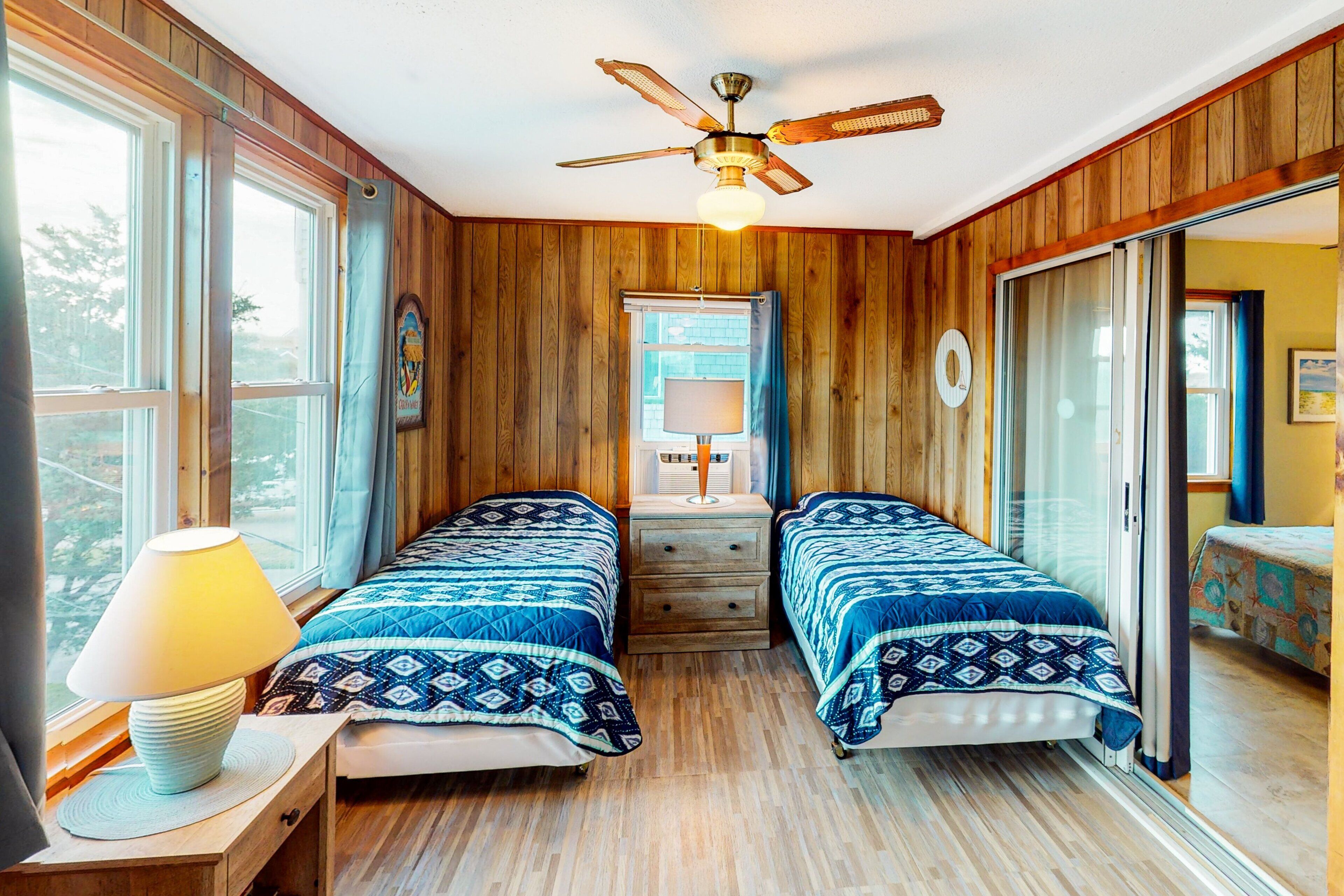 A room with two beds, a ceiling fan, a window, and a lamp.