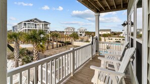 A wooden deck with white railings, overlooking a beach with palm trees and a pool. - Sunny Daze: Soundview, Private Pool, Elevator (Ocean Isle Beach)