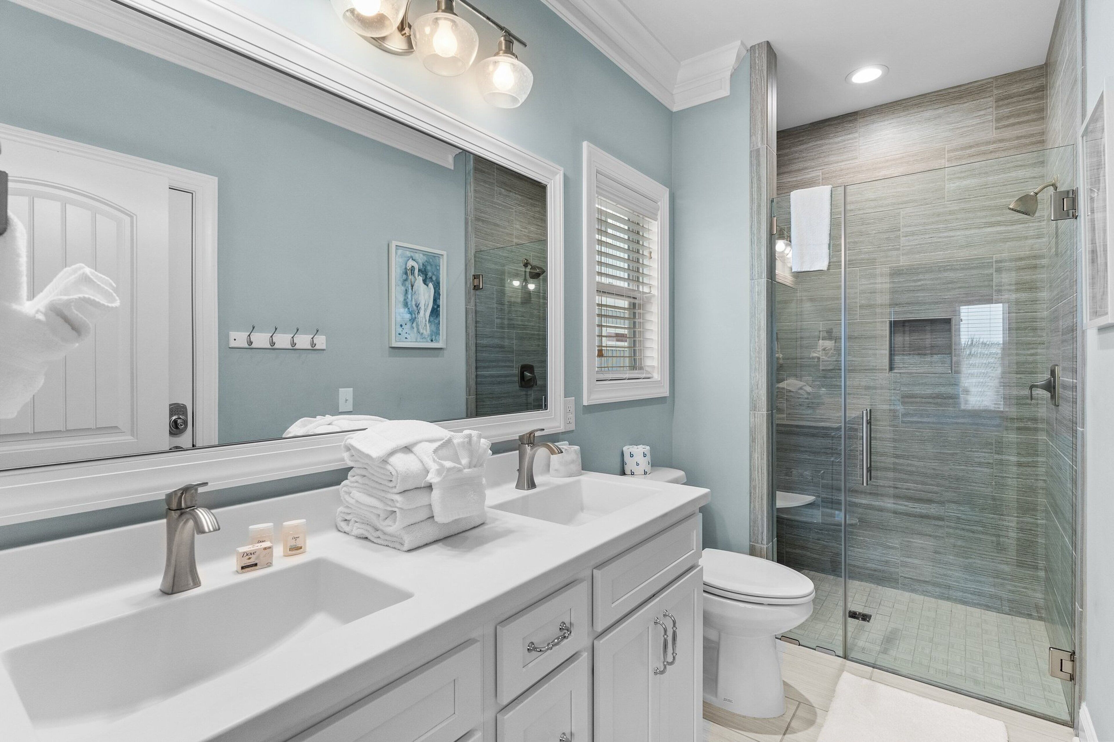 A modern bathroom with a large mirror, two sinks, a toilet, and a glass-enclosed shower.