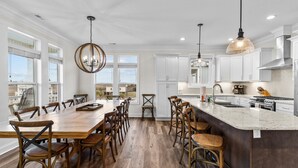 A spacious kitchen with a large island, wooden chairs, and pendant lighting. - Sunny Daze: Soundview, Private Pool, Elevator (Ocean Isle Beach)