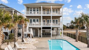 A two-story building with a pool, outdoor seating, and palm trees. - Sunny Daze: Soundview, Private Pool, Elevator (Ocean Isle Beach)