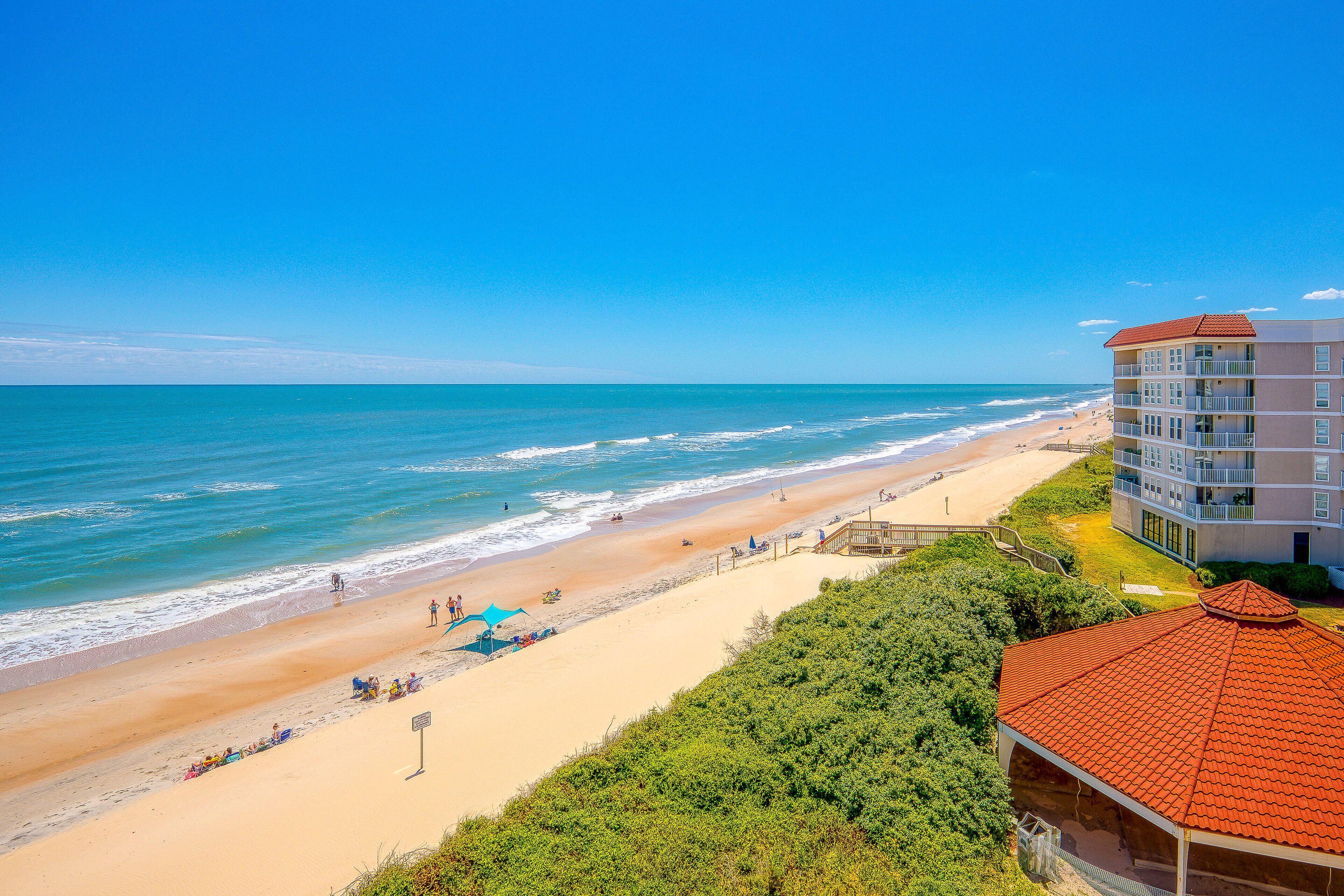 A beachfront hotel with a sandy beach, ocean view, and a building with multiple balconies.