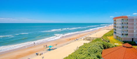 A beachfront hotel with a sandy beach, ocean view, and a building with multiple balconies.