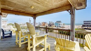 Een houten terras met gele Adirondack-stoelen en een bankje met uitzicht op een strand en de oceaan.