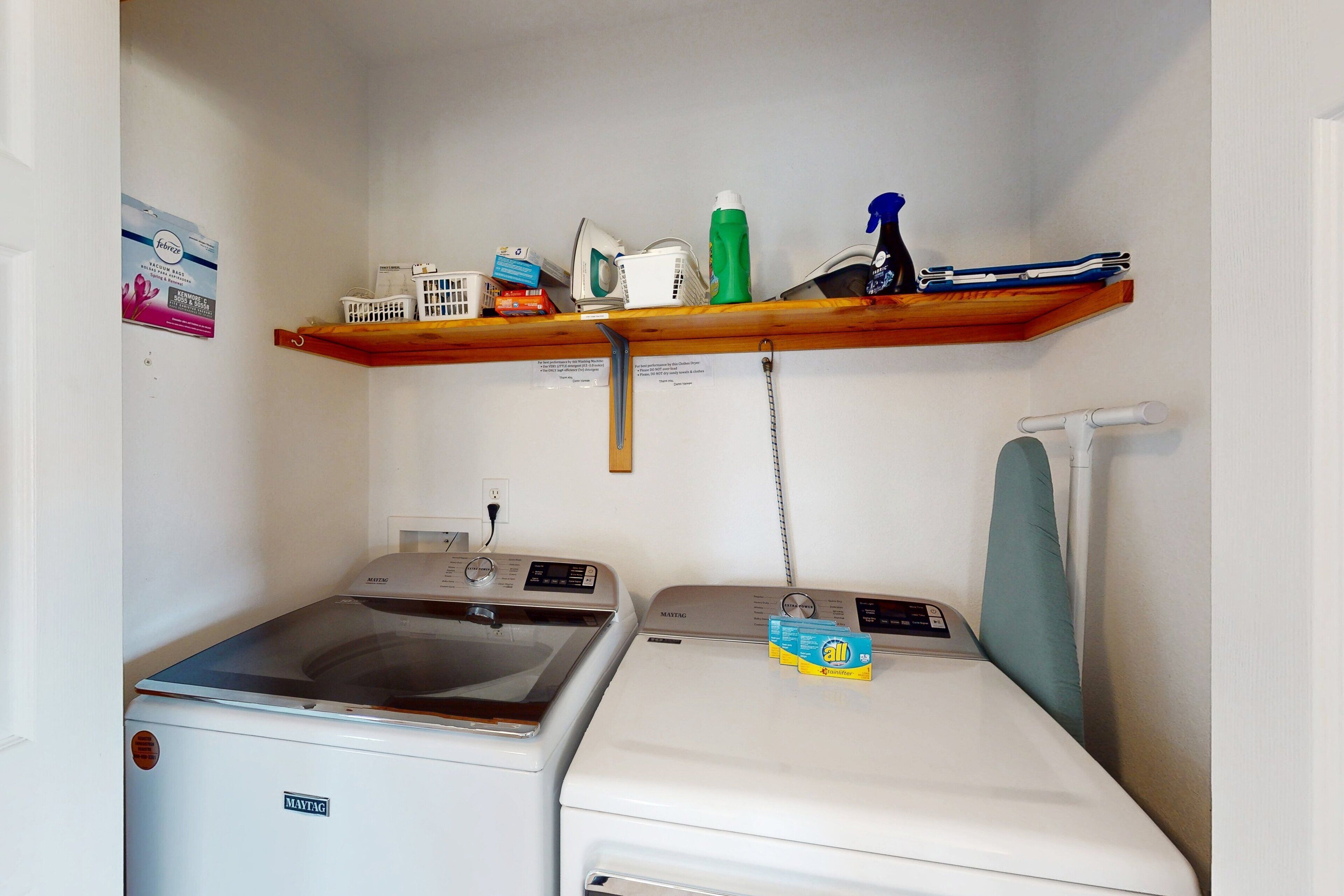 Un espace buanderie comprenant un lave-linge, un sèche-linge et une étagère au-dessus, où sont rangés les produits de nettoyage.