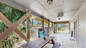 Un espacio al aire libre cubierto con un banco de madera, palmeras y vista a una casa al fondo.