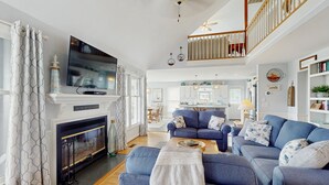 Una sala de estar con chimenea, sofás azules, un televisor y una escalera que lleva a un nivel superior.