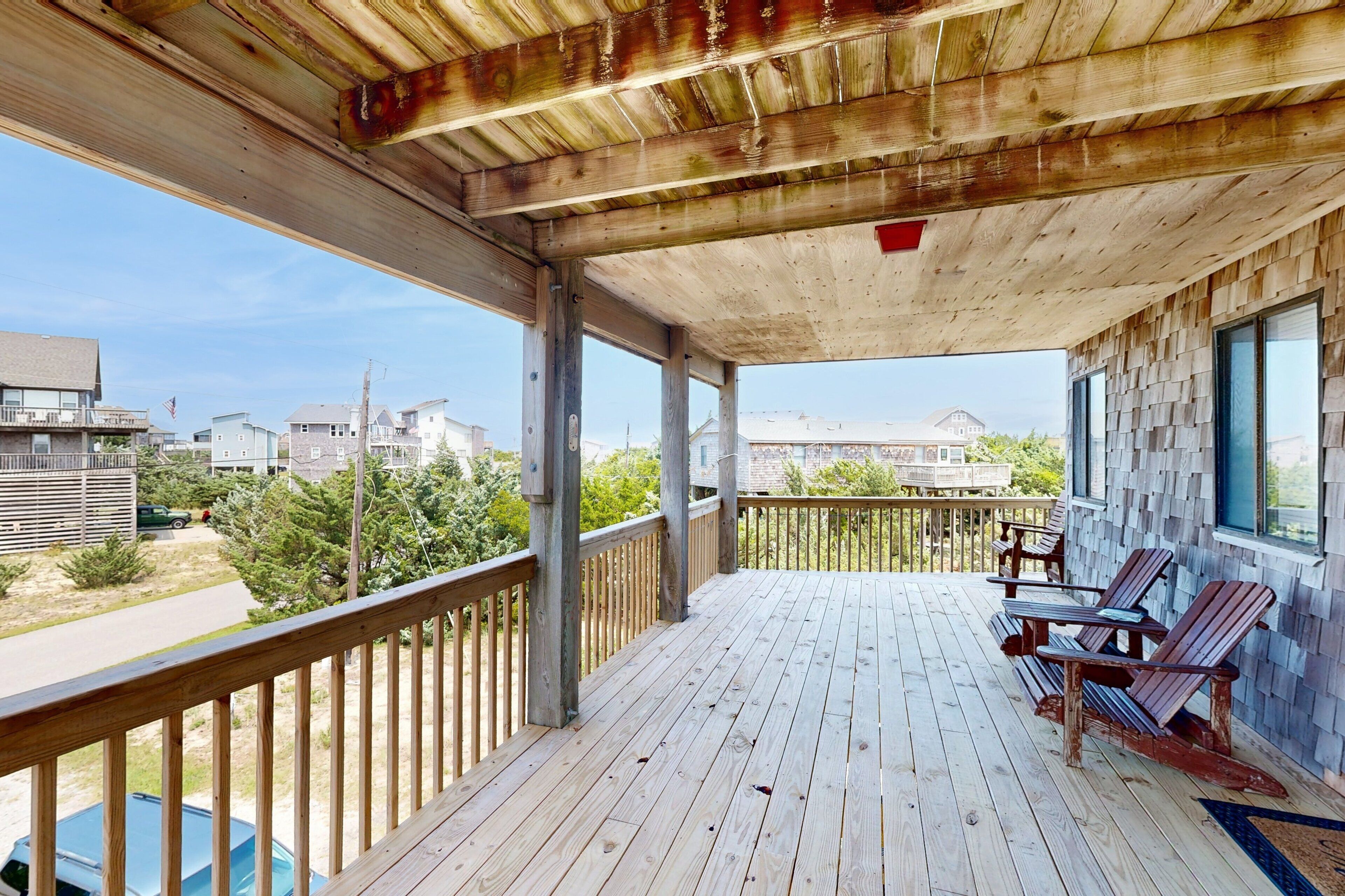 A wooden deck with a railing, a table, and four Adirondack chairs.