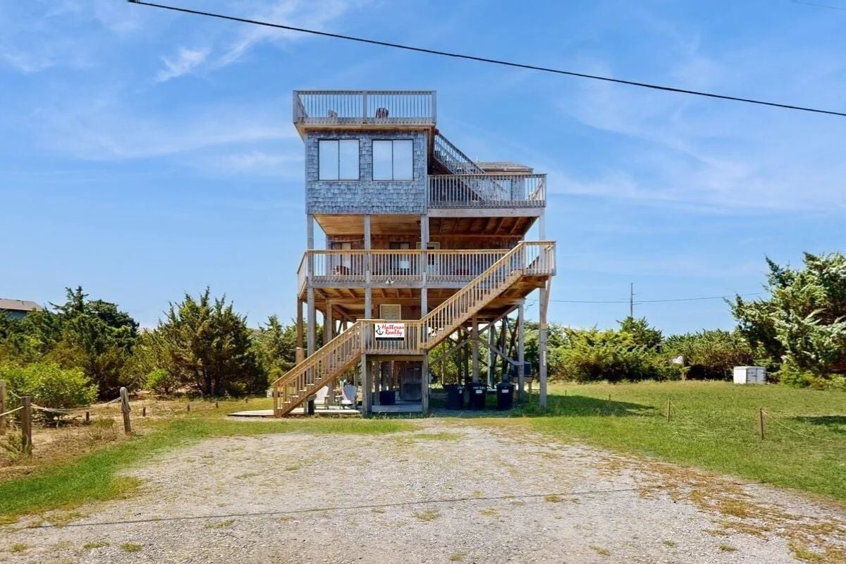 A multi-level wooden structure with a staircase leading to a balcony, surrounded by greenery.
